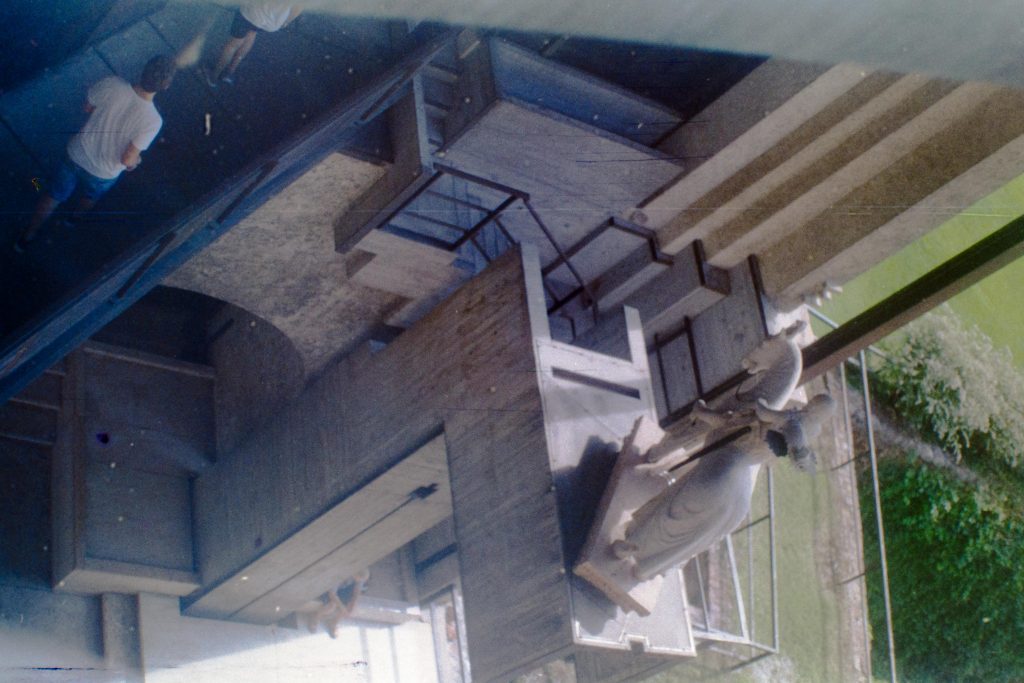 Confusing perspective on a stairway leading to a elevated passageway next to a statue in an historical building