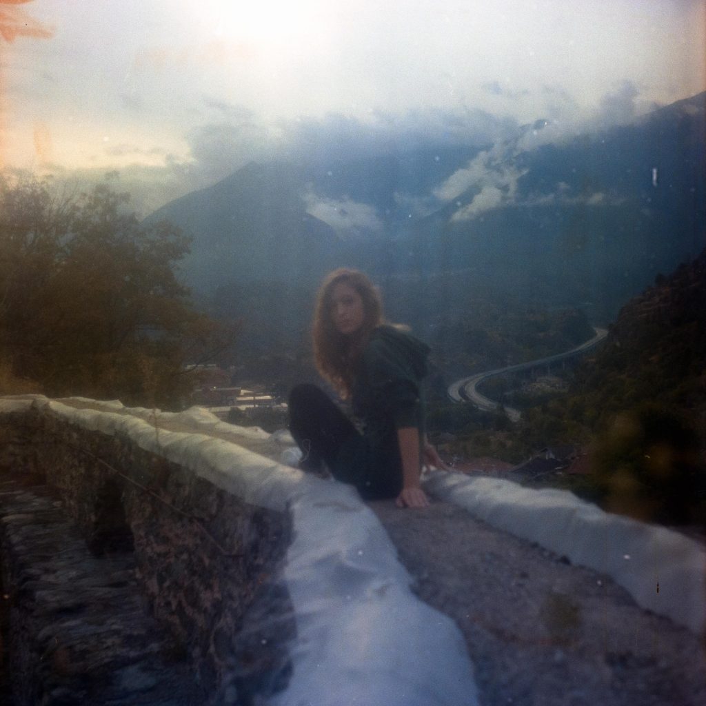 a girl sitting on a stone wall with a mountain scene in the background