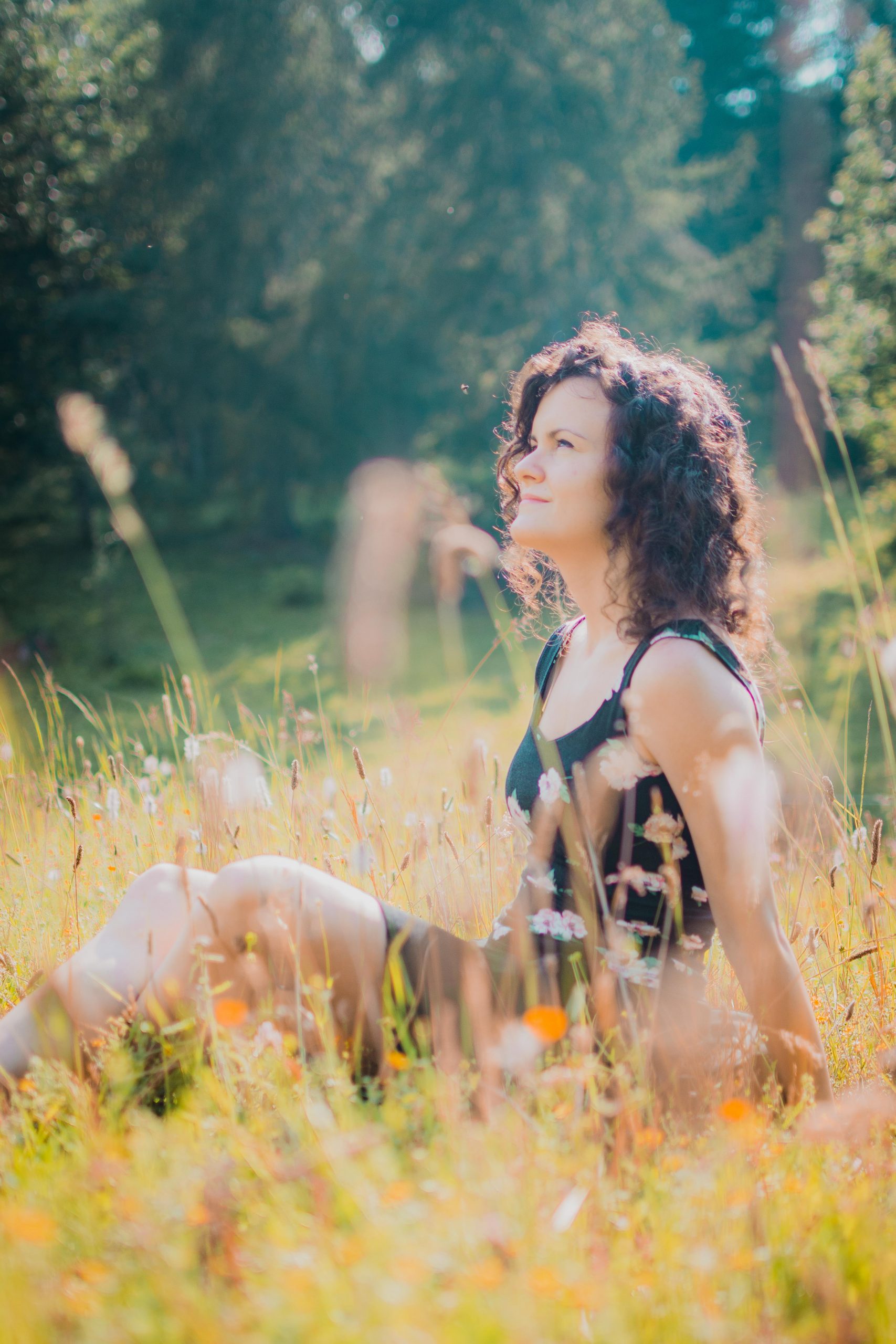 a girl with a black shirtless dress sitting in a field in the woods