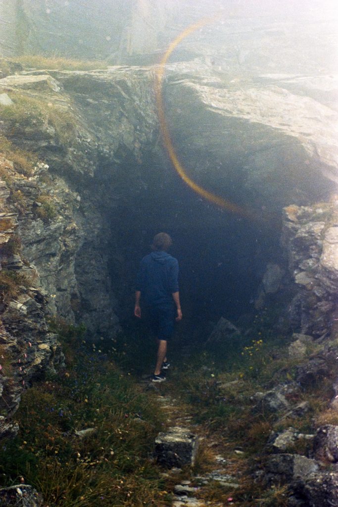 A Guy standing on a trail in front of a cave entrance with fog and film wear on top