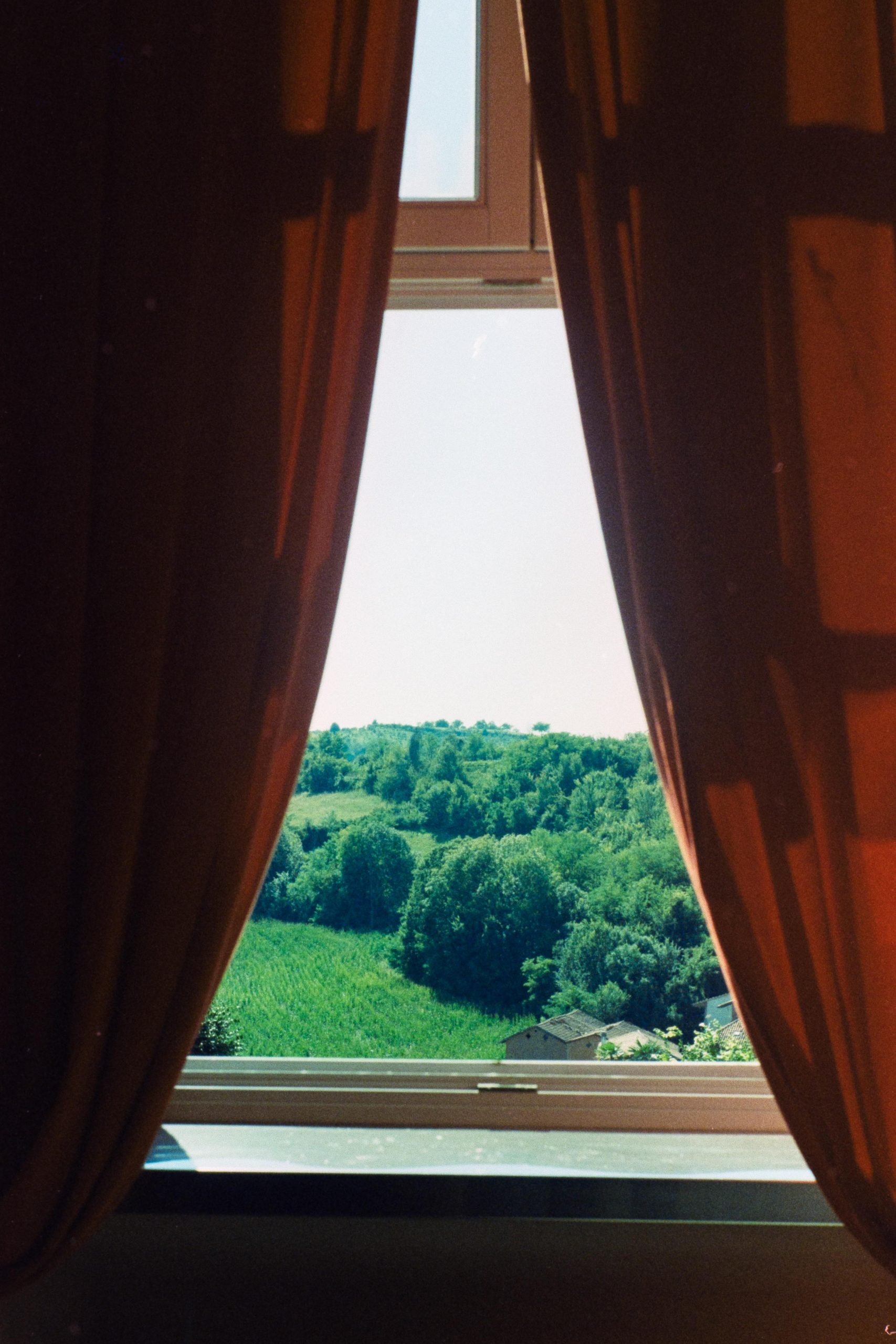 Red curtains covering a window in front of a hilly view