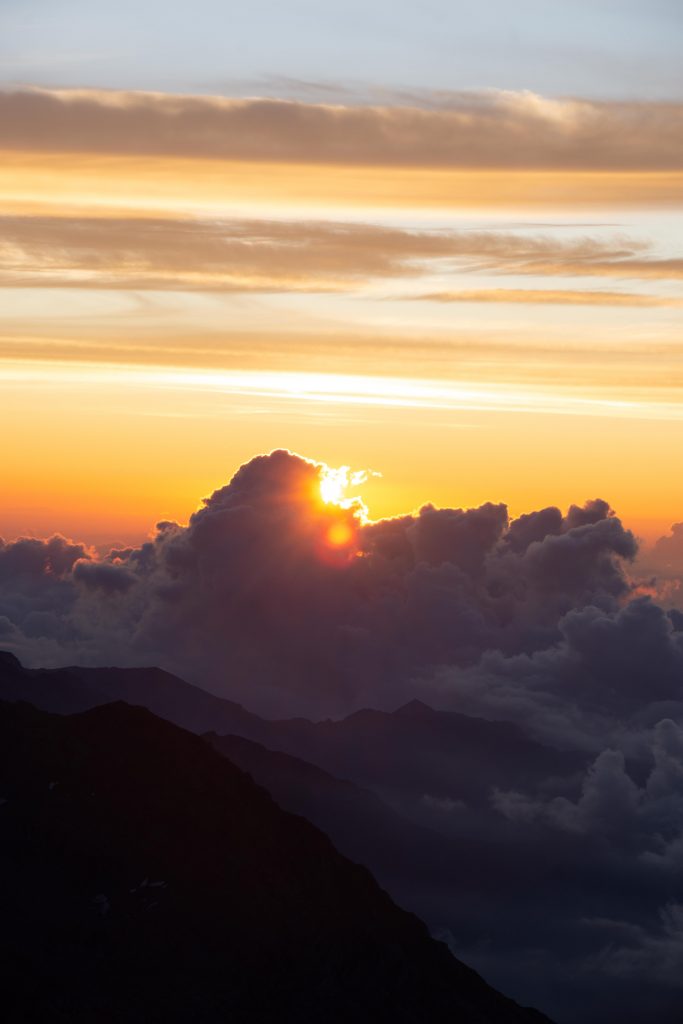 the Sun appearing from the clouds above some mounain tops