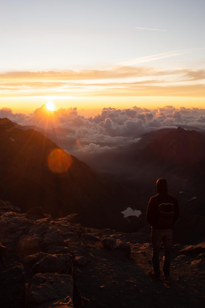 a guy looking at the sun rising on a sea of clouds