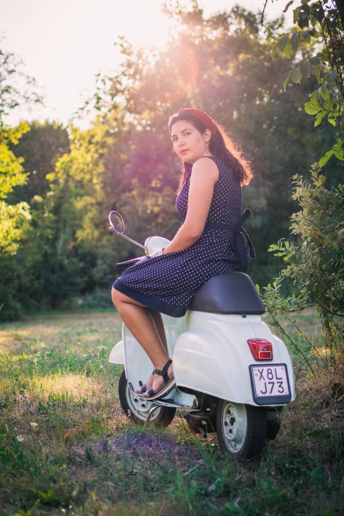 A girl vintage dressed sitting on a vintage Vespa