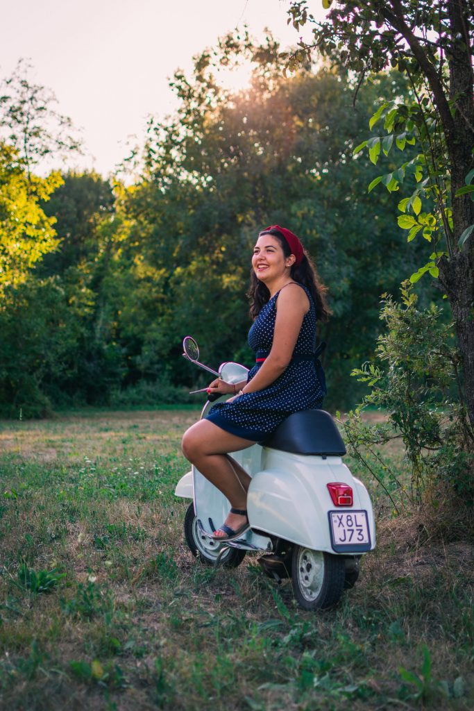 A girl vintage dressed sitting on a vintage Vespa