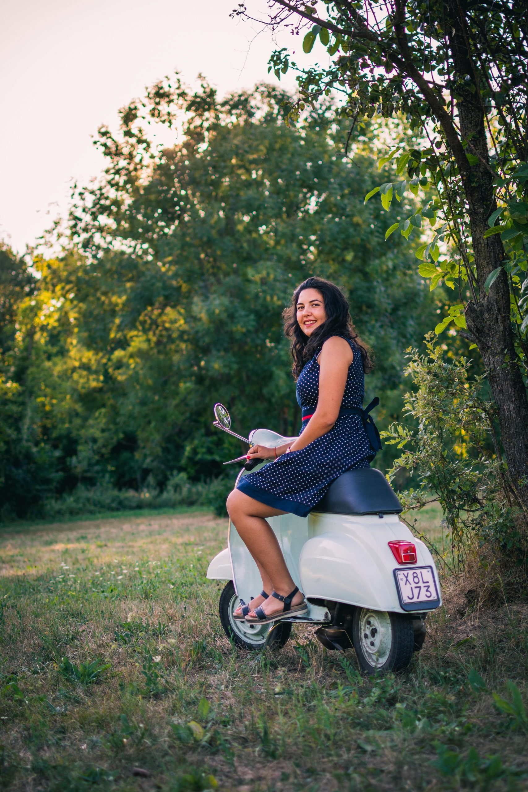 A girl vintage dressed sitting on a vintage Vespa