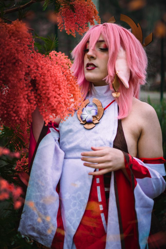 A girl dressed in a Yae Miko Cosplay looking at some pink flowers